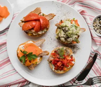 plato blanco con cuatro tostadas de pan redondo pequeño con ingredientes diferentes