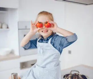 niña en una cocina jugando con dos tomates como si fueran ojos