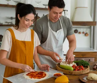 mujer y hombre sonrientes preparando una pizza en una cocina de casa